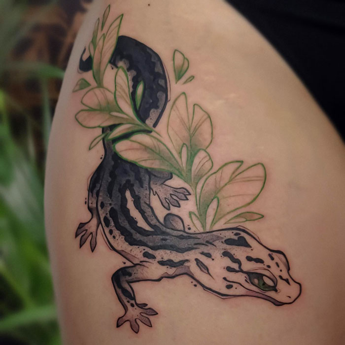 Animal tattoo featuring a stylized lizard intertwined with green leaves on skin.
