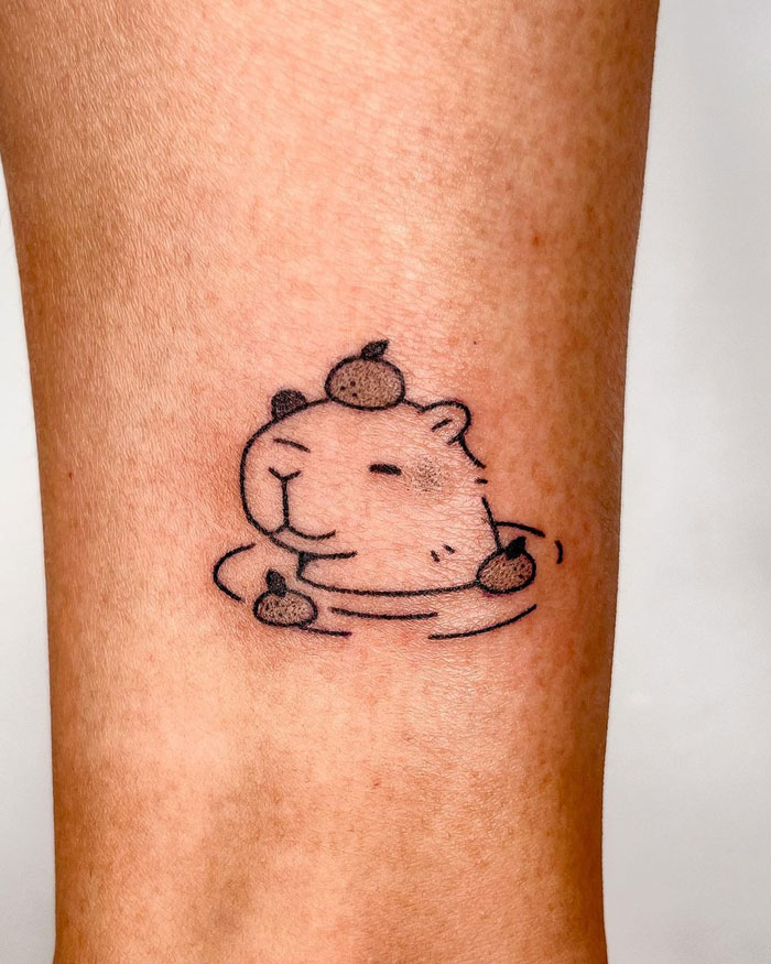 Animal tattoo of a capybara relaxing in water with small fruits on its head, showcasing creative design.