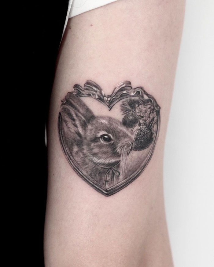Simple and realistic animal tattoo of a rabbit inside a heart-shaped frame on an arm.