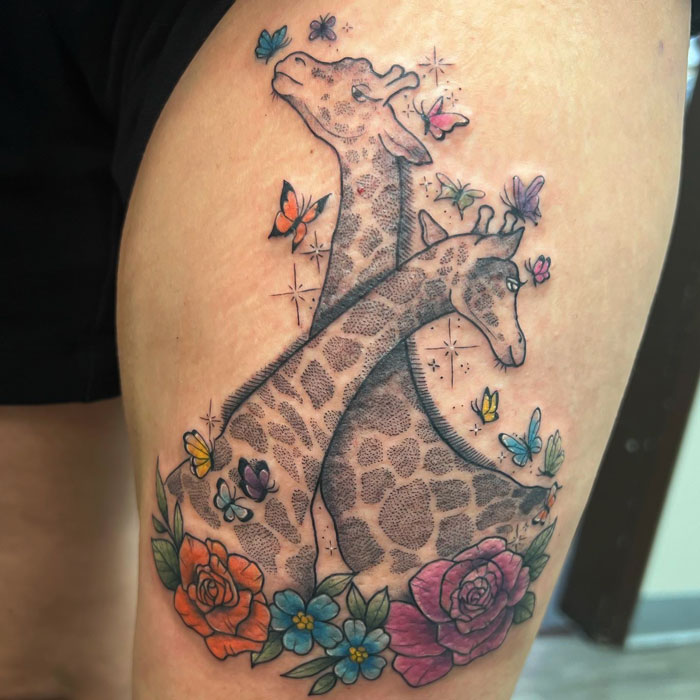 Giraffe tattoo with butterflies and flowers, showcasing animal tattoo artistry on the upper thigh.