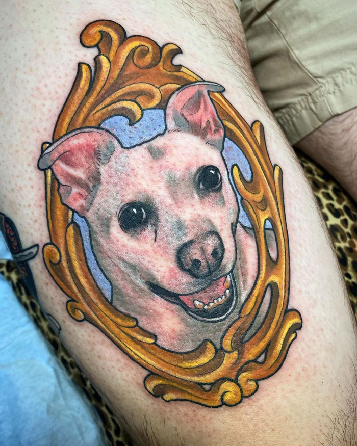 Realistic animal tattoo of a dog's portrait framed in ornate gold design on skin, showcasing simplicity and detailed realism.