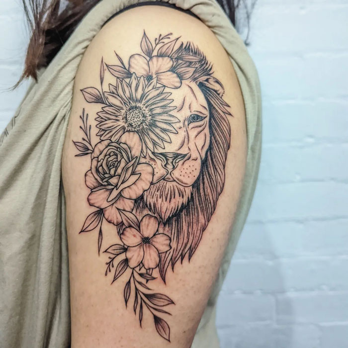 Lion and floral tattoo on upper arm, featuring detailed linework and blooming flowers.