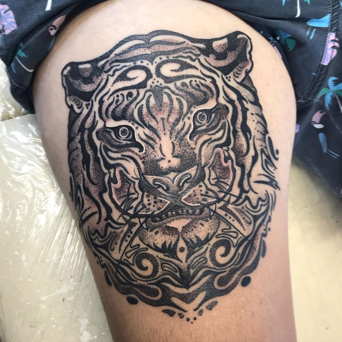 Intricate animal tattoo of a tiger face on the thigh, showcasing detailed linework and shading.