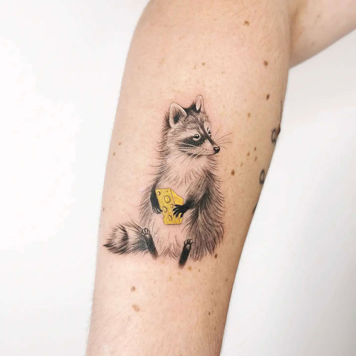 Animal tattoo of a raccoon holding cheese on arm, showcasing creative design ideas.