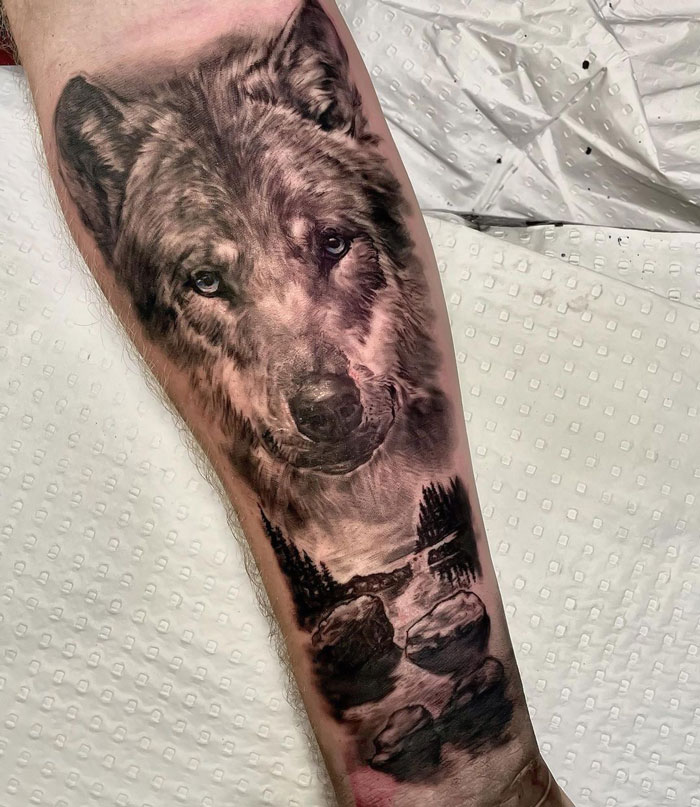 Wolf tattoo on forearm with detailed forest landscape, showcasing creative animal tattoo ideas.
