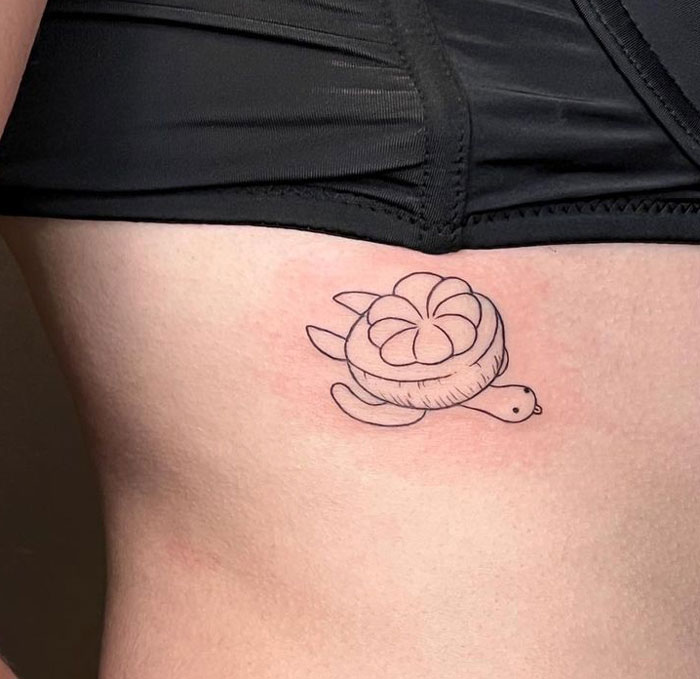 Minimalist animal tattoo of a turtle with a flower shell on the side of a person's torso, near a black waistband.