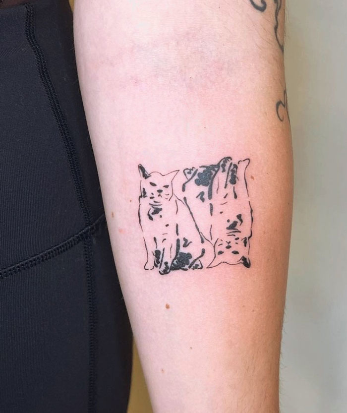 Animal tattoo of two abstract cats on forearm.