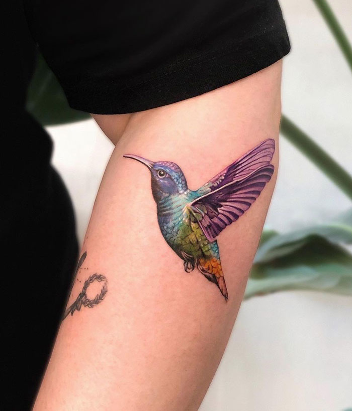 Colorful hummingbird tattoo on an arm, showcasing animal kingdom art with vibrant detail.