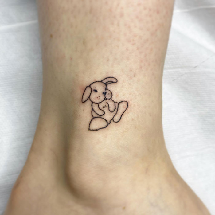 Minimalist animal tattoo of a cute bunny on a person's ankle.