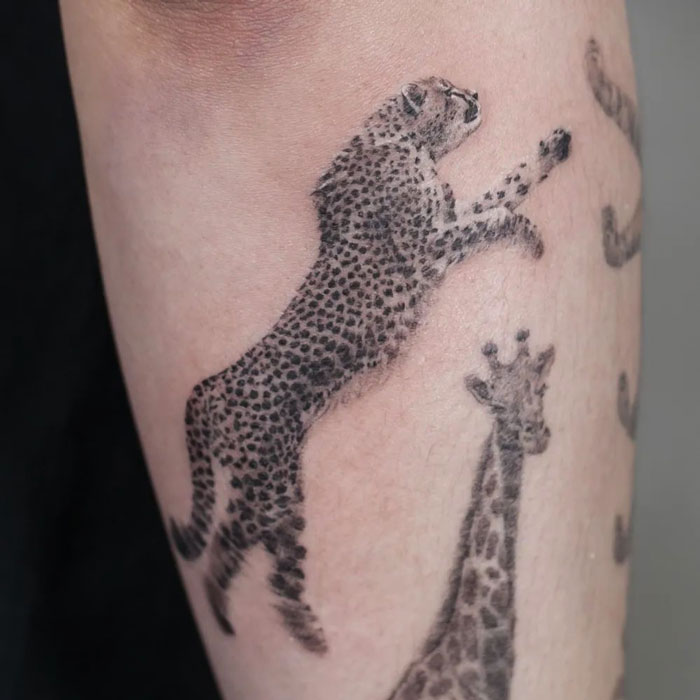 Tattoo of a leaping cheetah and a giraffe on forearm, celebrating the animal kingdom.