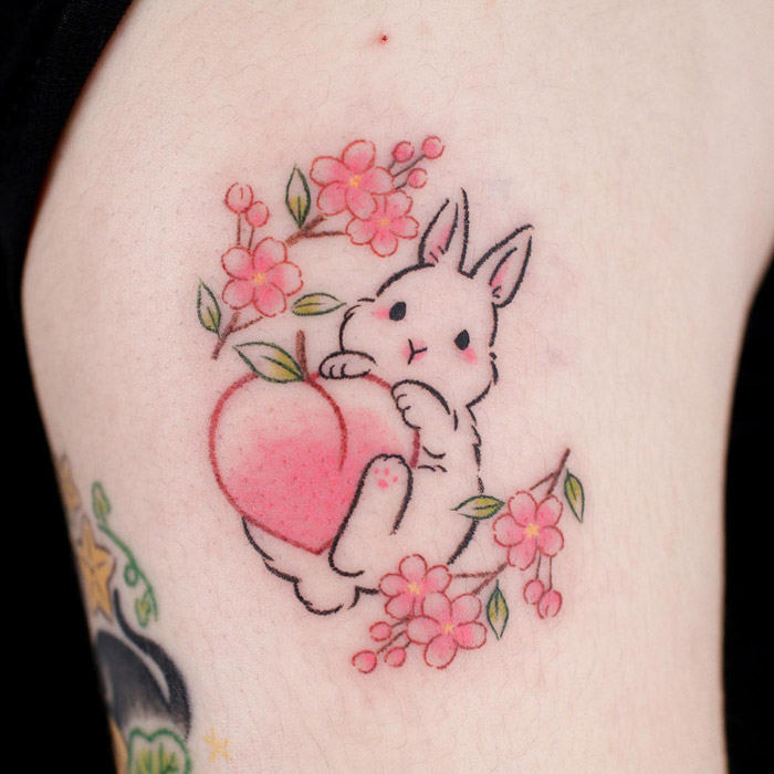 Cute bunny tattoo with a heart and pink flowers on skin, inspired by animal tattoo ideas.