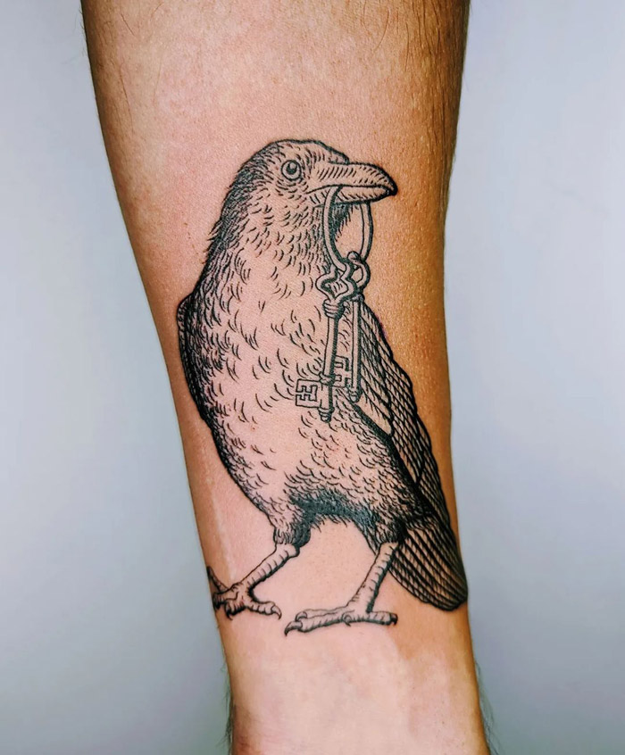 Crow tattoo holding a key on arm, celebrating the animal kingdom.