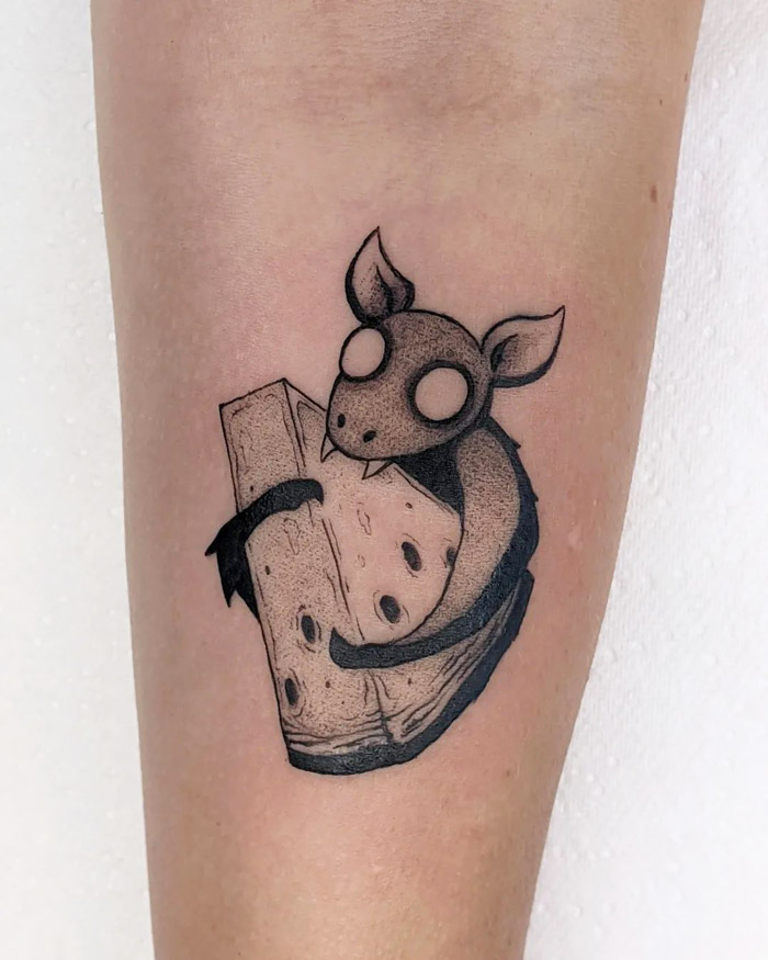 Animal tattoo of a stylized bat holding a piece of cheese, inked on the forearm.