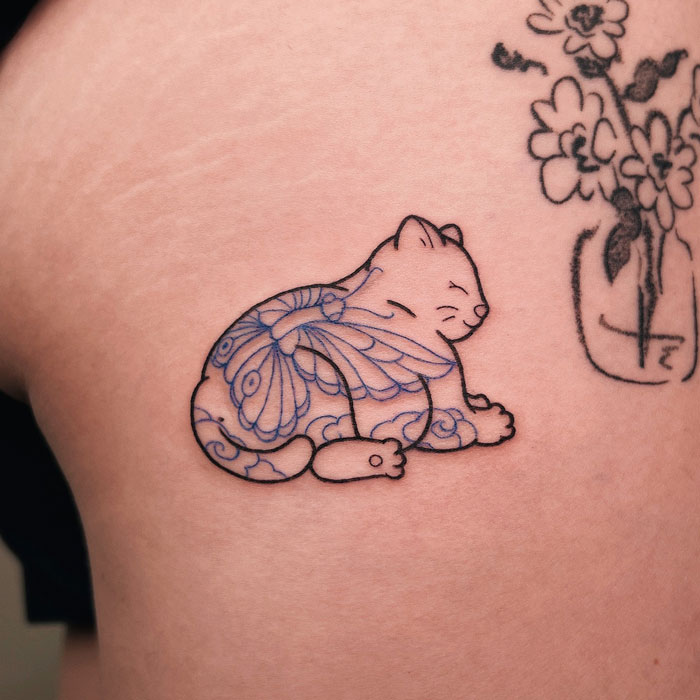 Stylized animal tattoo of a sleeping cat with intricate line patterns on a person's skin.