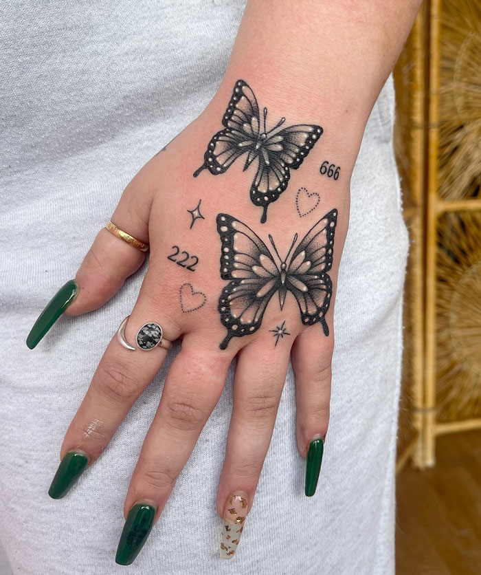 Butterfly animal tattoo on hand with numbers and heart designs, featuring green nail polish.