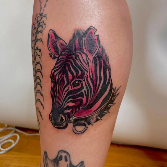 Zebra tattoo showcasing realistic animal design on a person's arm, featuring linear patterns and spiked collar.