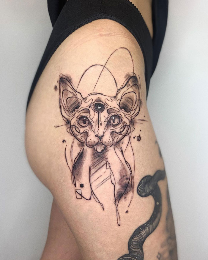 Abstract animal tattoo of a cat with three eyes on a person's leg.