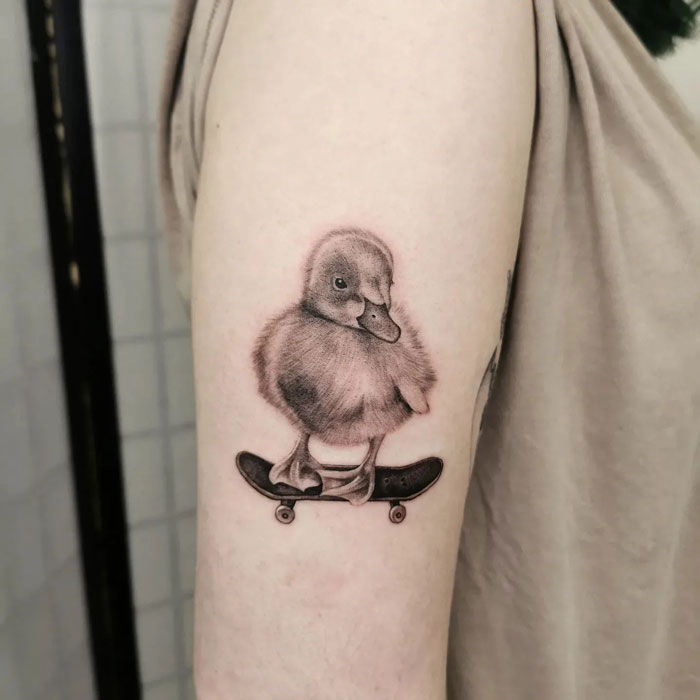 Duckling tattoo on arm, featuring a cute design of a duck on a skateboard, showcasing unique animal tattoo art.