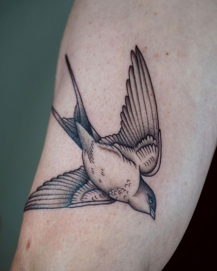 Tattoo of a bird in flight on an arm, showcasing animal kingdom artistry with intricate details and shading.