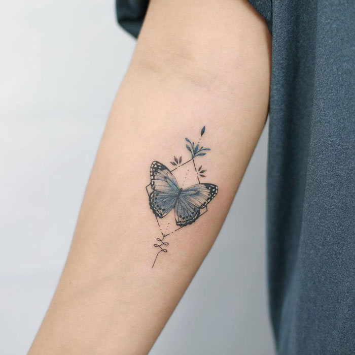 Butterfly tattoo on forearm embodying simplicity and realism with delicate floral design.