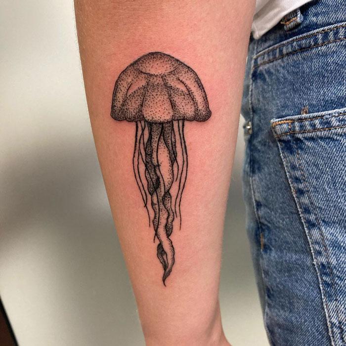 Jellyfish tattoo on person's forearm, showcasing creative animal tattoo ideas against a denim backdrop.