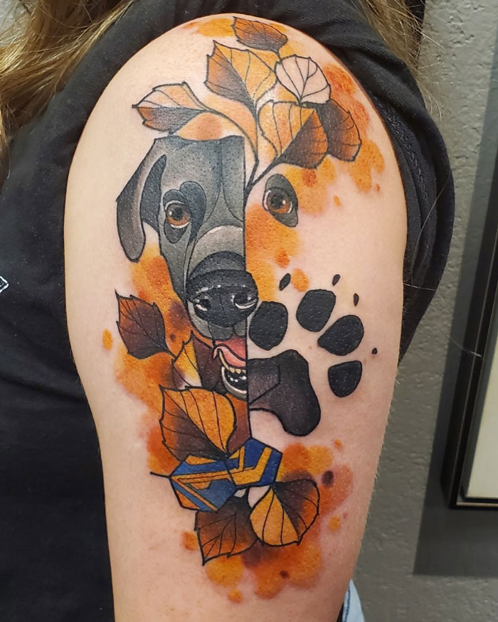 Animal tattoo of a dog surrounded by leaves and paw print, showcasing vibrant colors and intricate design on an arm.