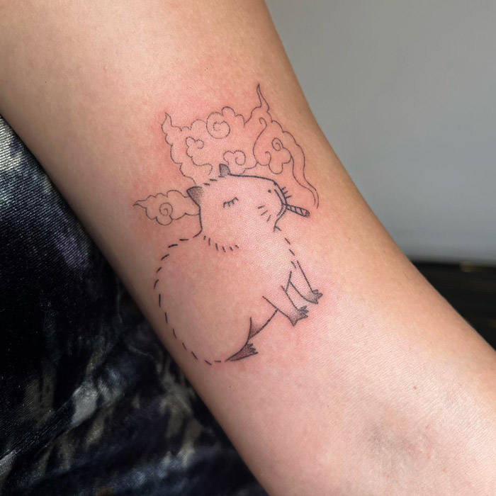 Simple and realistic animal tattoo of a small, stylized creature with clouds, inked on an arm.