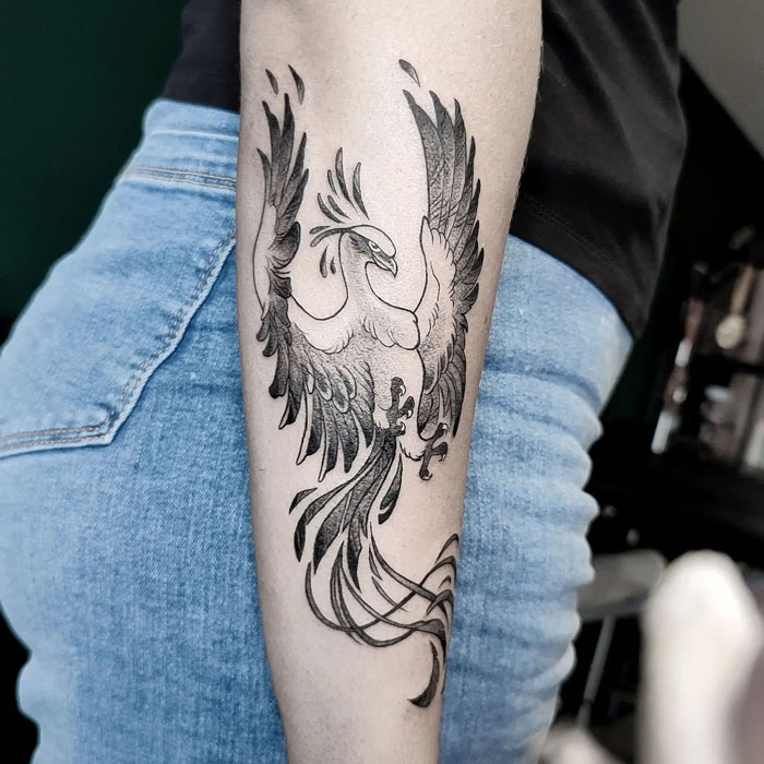 Phoenix animal tattoo on forearm, featuring detailed wings and tail in black ink.