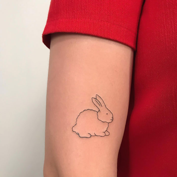 Minimalist rabbit animal tattoo on arm in red shirt.
