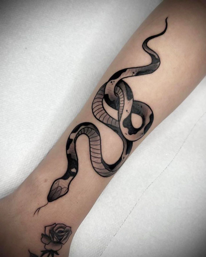 Snake tattoo design on an arm, showcasing intricate animal tattoo art, with a small rose inked nearby.
