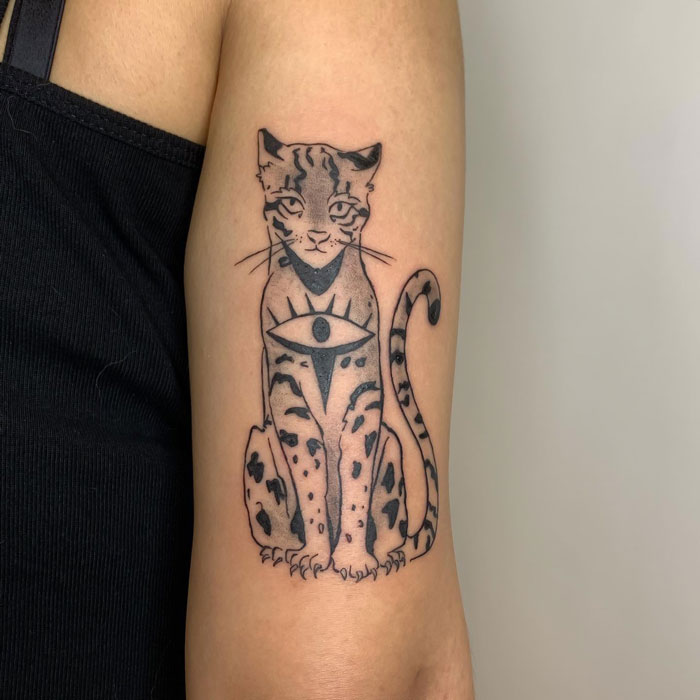 Detailed animal tattoo of a sitting feline with an eye on its chest, inked on a person's arm.