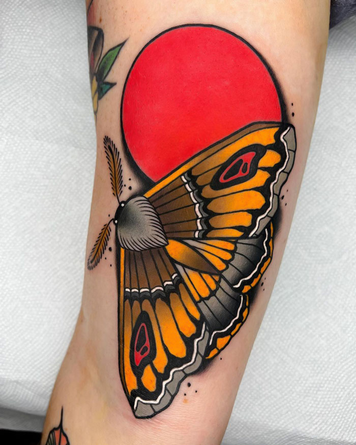 Colorful moth tattoo featuring bold orange and black wings, set against a red circle, showcasing creative animal tattoo ideas.