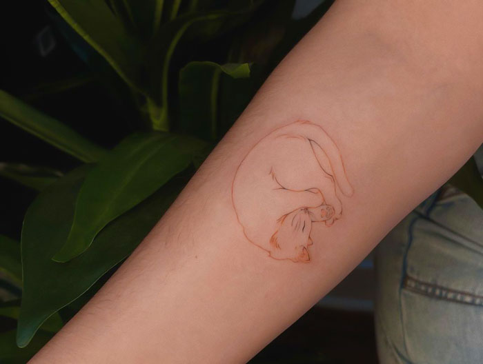Minimalist cat tattoo on forearm, with leaves in the background, highlighting trendy animal tattoo ideas.