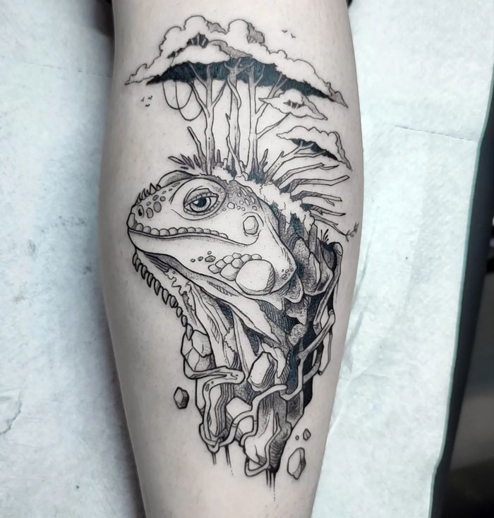 Animal tattoo of a detailed iguana with trees on a leg.