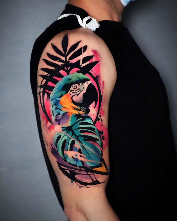 Colorful parrot tattoo on a person's arm, featuring vibrant hues and abstract leaf designs, celebrating the animal kingdom.