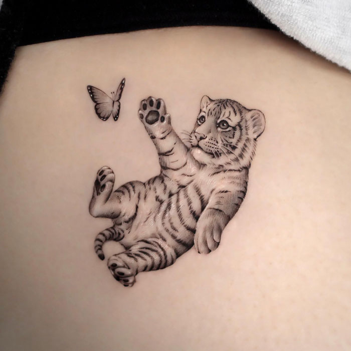 Realistic animal tattoo of a playful tiger cub reaching for a butterfly, embracing simplicity.