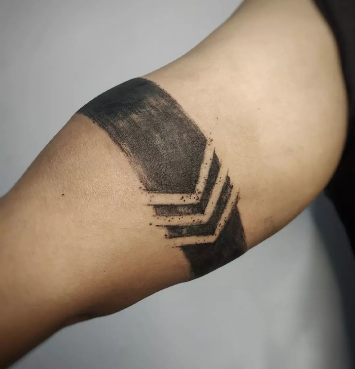 A geometric black armband tattoo design with chevron patterns on a person's arm.