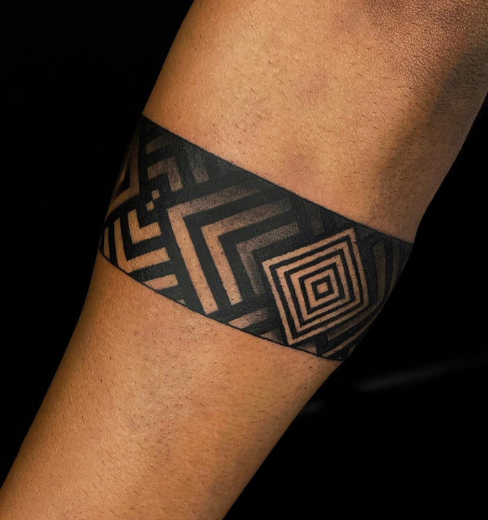 Geometric patterned armband tattoo on forearm, showcasing bold black lines and intricate design.