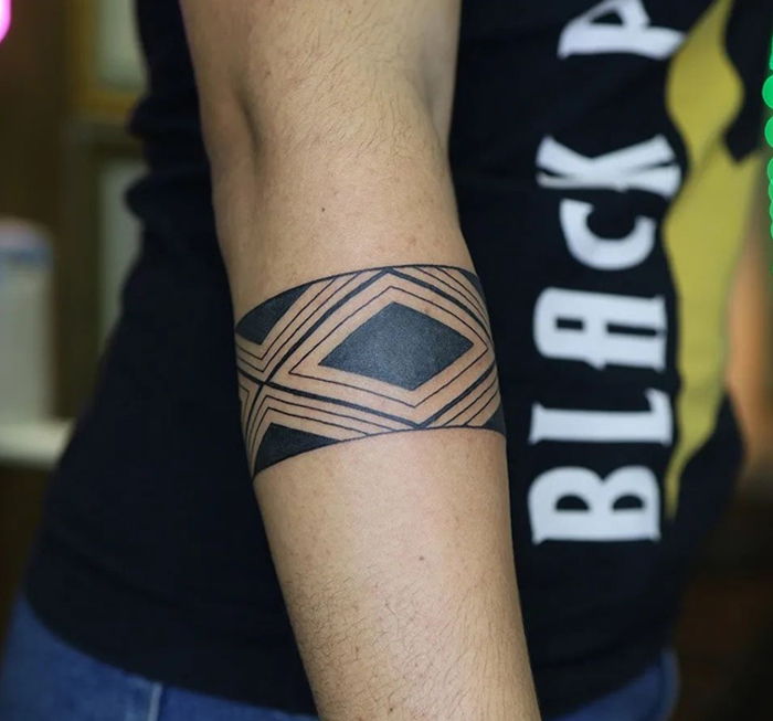 Geometric armband tattoo design on a person's forearm, showcasing intricate patterns and bold lines.