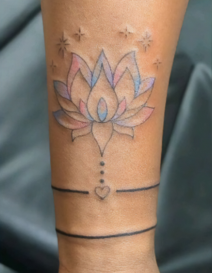 Armband tattoo featuring a colorful lotus design with stars, a heart, and elegant lines, symbolizing peace and purity.