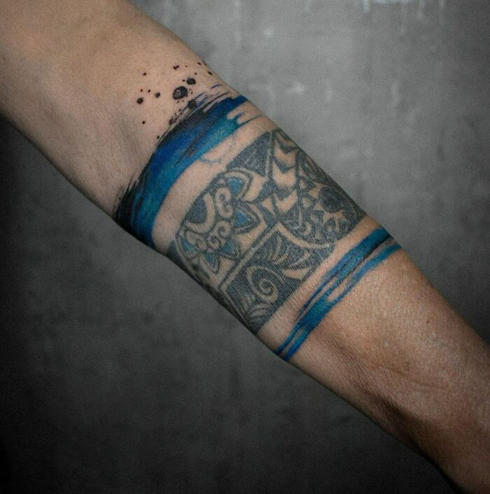 Armband tattoo design with intricate black and blue patterns on a person's forearm.