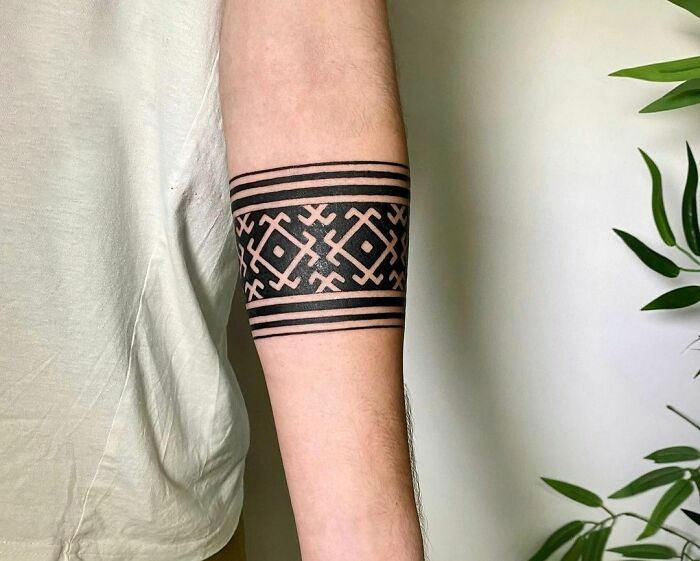 Ornate black armband tattoo design on a person's forearm, featuring geometric patterns.