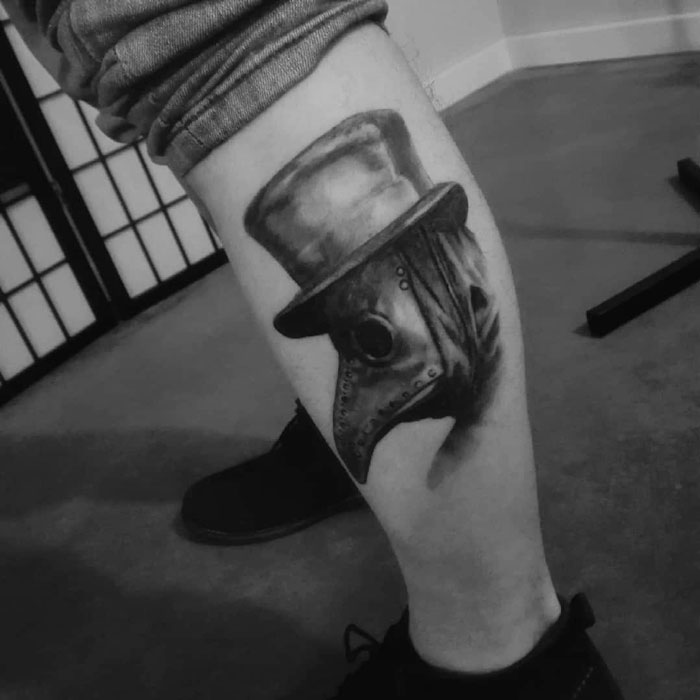 Calf tattoo featuring a detailed plague doctor in a top hat, showcasing coolness and intricate artistry.