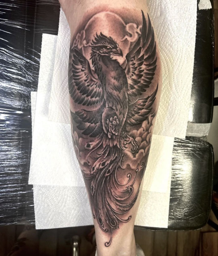 Lower leg tattoo featuring a detailed blackwork phoenix design.