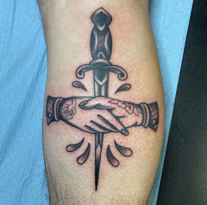Lower leg tattoo of two shaking hands over a dagger with intricate details.