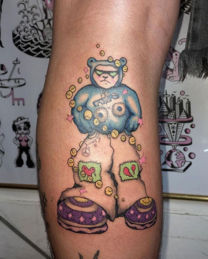 Colorful teddy bear calf tattoo featuring patches, smiley faces, and vibrant shoes, showcasing unique tattoo artistry.