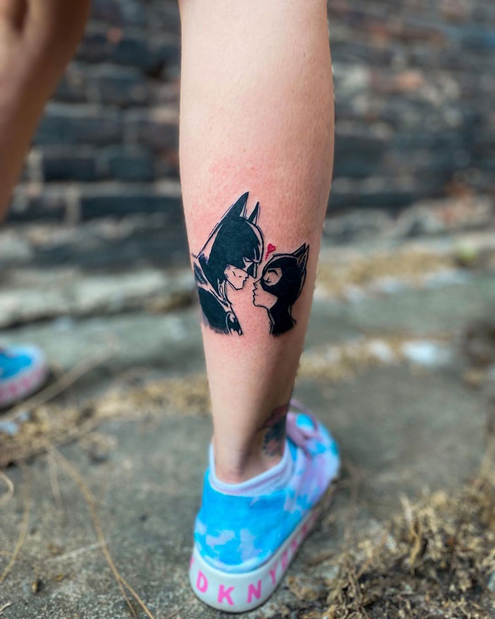 Lower leg tattoo featuring a stylized design of two masked characters facing each other.