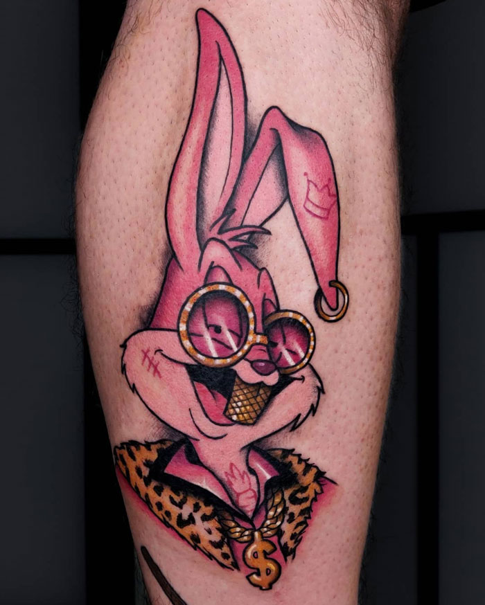 Colorful cartoon rabbit tattoo on calf with sunglasses and leopard print collar, showcasing coolness.
