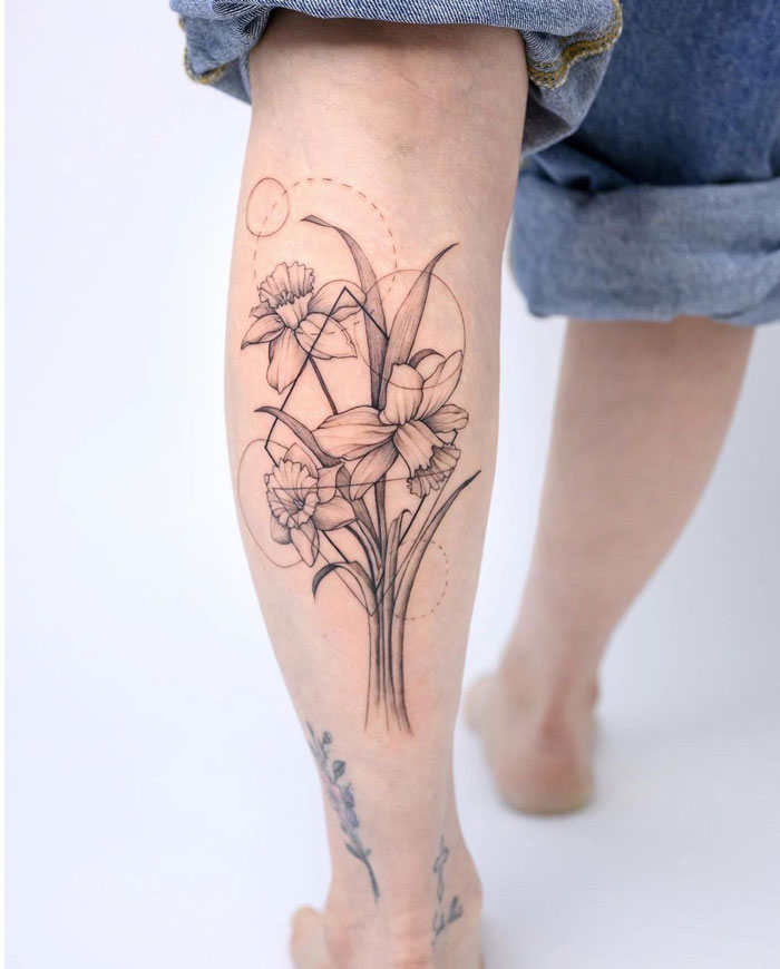 Delicate floral calf tattoo design showcasing daffodils in black ink, epitomizing coolness and artistic flair.