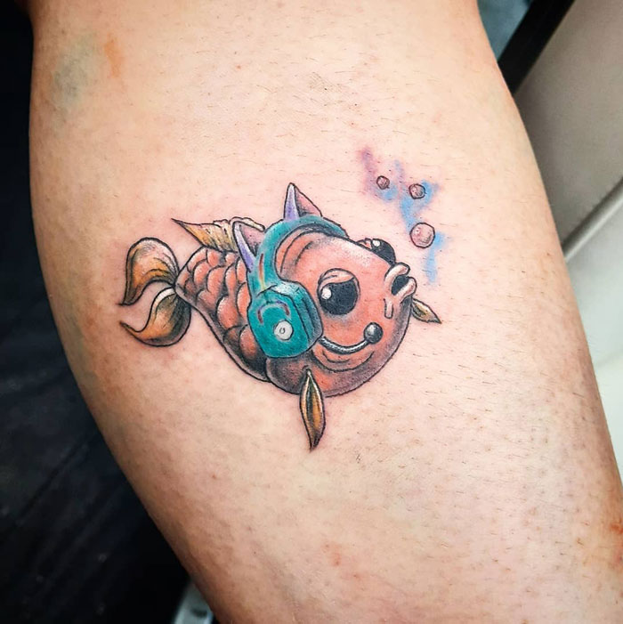 Lower leg tattoo of a colorful fish with headphones, emitting bubbles.